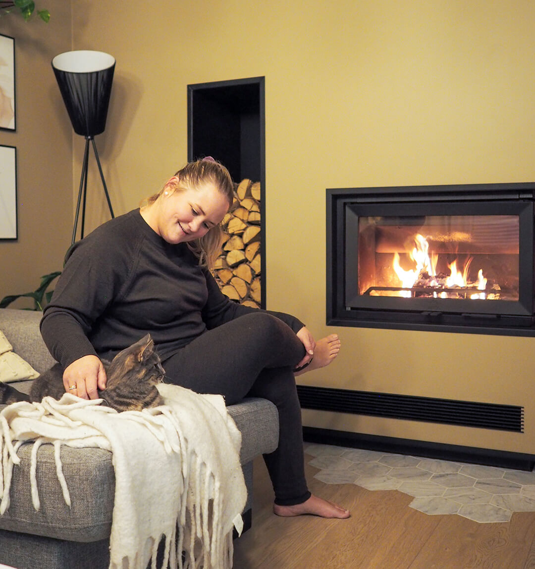 Karoline sitting on the sofa with her cat in front of the Jøtul I 620 FR fireplace insert