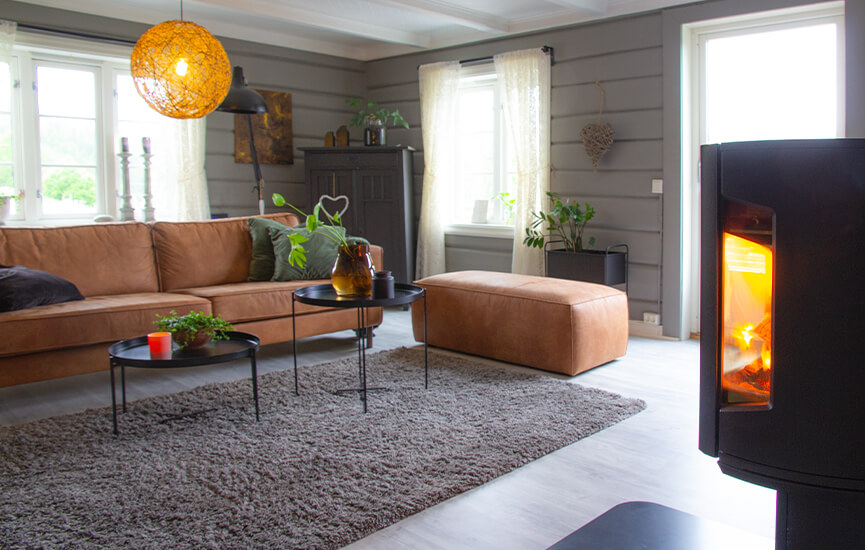 Wood stove in gray living room with timber walls and brown sofa