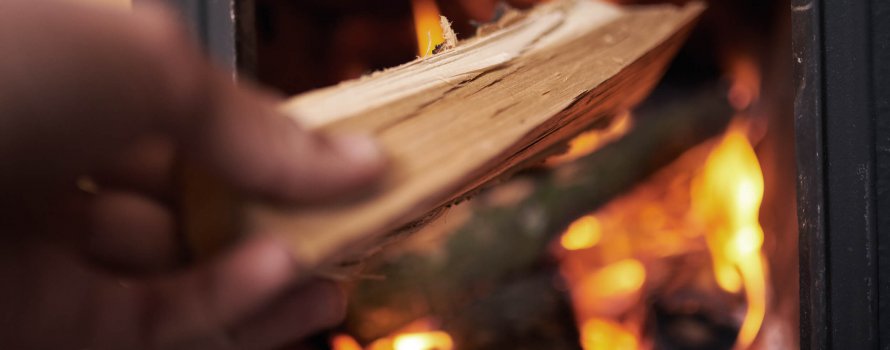 The hand which hold the wood and putting it into fireplace