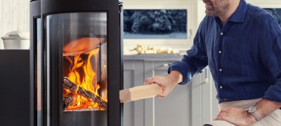 A man puts firewood in a wood burning stove Jøtul F 373 Advance 