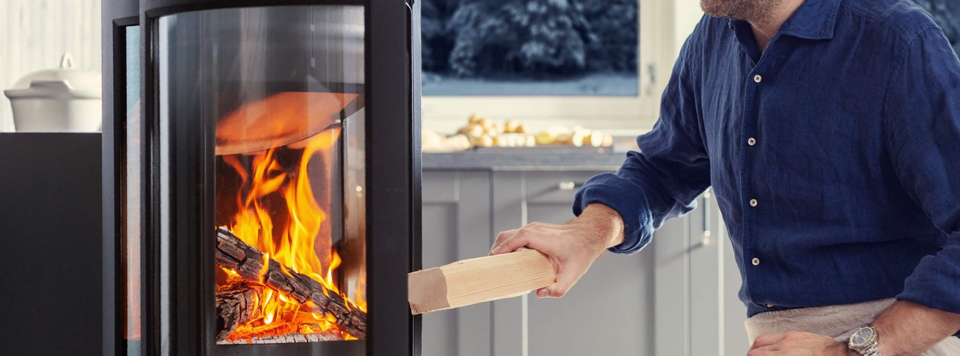 A man puts firewood in a wood burning stove Jøtul F 373 Advance 