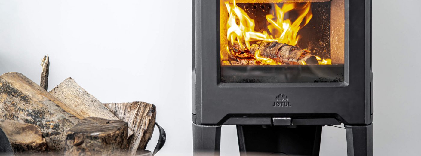 Jøtul F 163 black wood stove with logs on the side and white wall at the back 