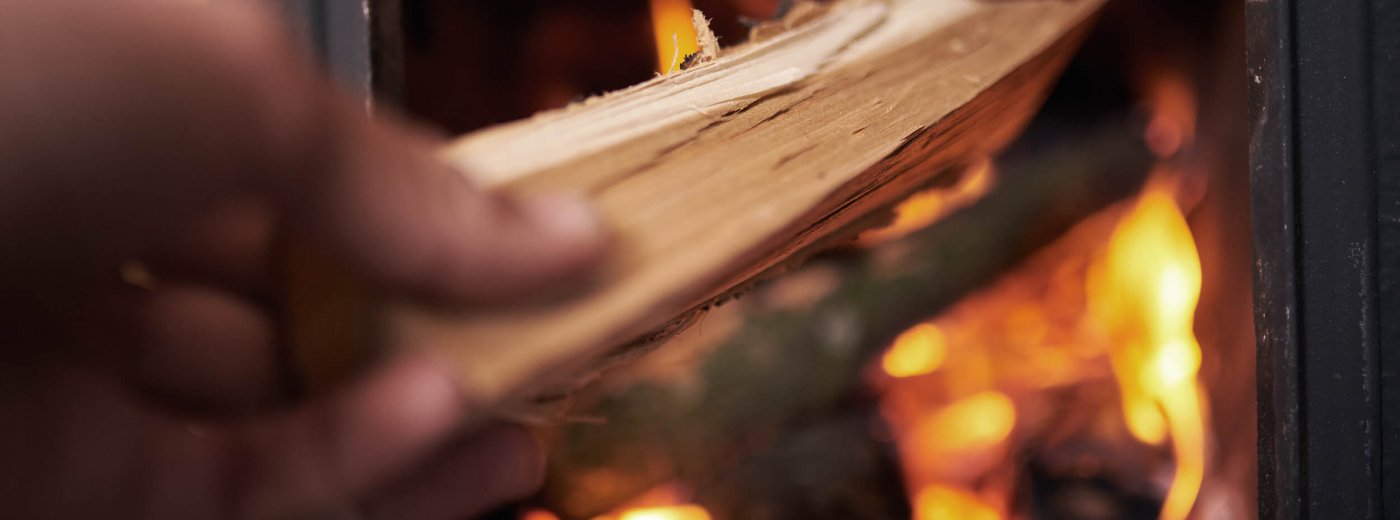 The hand which hold the wood and putting it into fireplace
