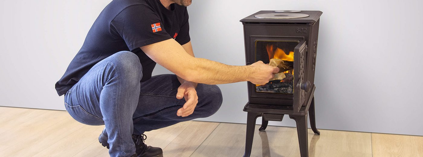 A man adding firewood into the wood stove Jøtul F 602
